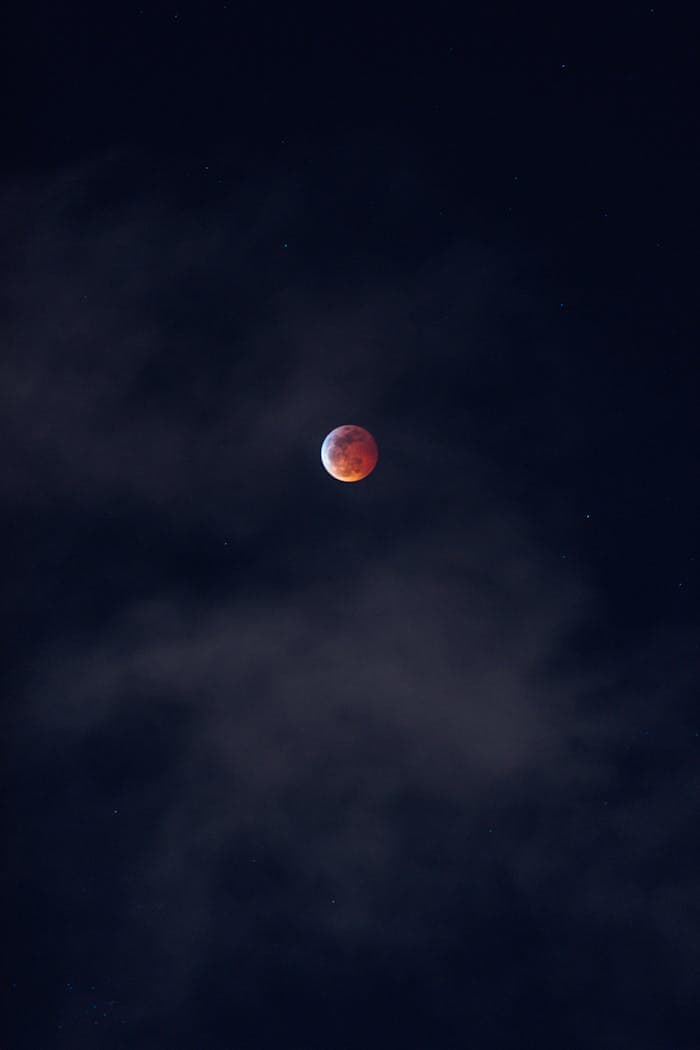 Stunning blood moon captured in a starry night sky with dark clouds.